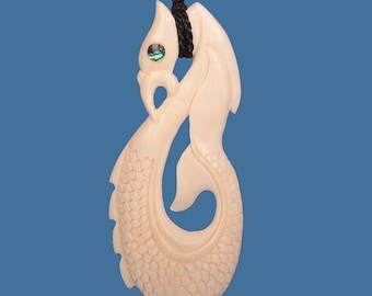 May include: Ivory-colored pendant necklace featuring a stylized fish design. The pendant is carved with intricate details, including scales and fins. A small, iridescent accent is set near the top. The necklace has a black cord.
