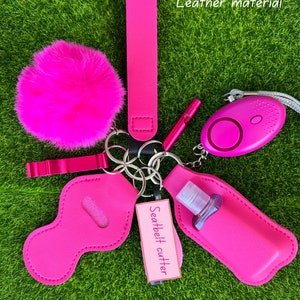 Può includere: Una collezione di accessori rosa acceso, tra cui un soffice pompon, un cinturino da polso, un fischietto, un allarme personale, un taglia cinture e un porta igienizzante per le mani. Gli articoli sono in materiale di pelle e sono attaccati a portachiavi.