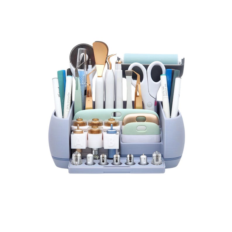 May include: A light blue craft organizer filled with various tools. The organizer has multiple compartments holding pens, scissors, tweezers, and other crafting essentials. Gold and white tools are visible, along with a blue roller and a variety of small, gold-topped containers.