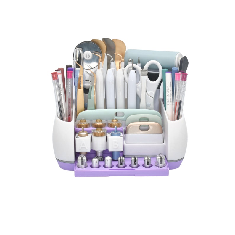 May include: A white and purple craft tool organizer filled with various tools, including pens, tweezers, scissors, and scrapers. The organizer has multiple compartments and a base with adjustable components. The tools are arranged neatly, suggesting a focus on organization and precision.