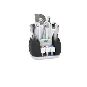 May include: A black and white craft organizer filled with various tools, including pens, scissors, and cutting blades. The organizer has a curved design with multiple compartments and a white base. The tools are neatly arranged, suggesting a focus on organization and crafting.