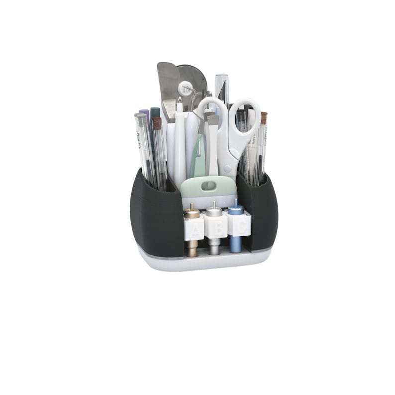 May include: A black and white craft organizer filled with various tools, including pens, scissors, and cutting blades. The organizer has a curved design with multiple compartments and a white base. The tools are neatly arranged, suggesting a focus on organization and crafting.