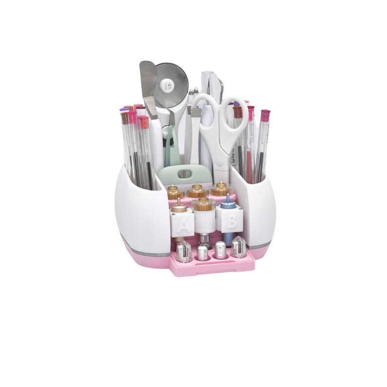 Puede incluir: Un organizador de manualidades blanco y rosa lleno de varias herramientas, incluyendo tijeras, bol&iacute;grafos y un cortador rotatorio. El organizador tiene m&uacute;ltiples compartimentos y una base rosa, ideal para guardar suministros de manualidades.