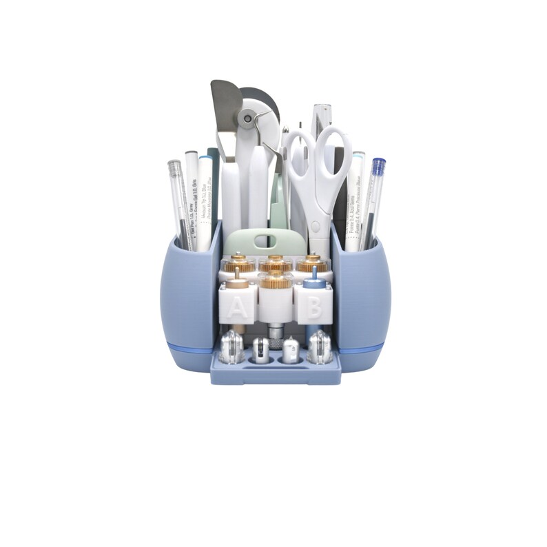 Puede incluir: Un organizador de manualidades azul claro lleno de varias herramientas, incluyendo bol&iacute;grafos, tijeras y una esp&aacute;tula. El organizador tiene m&uacute;ltiples compartimentos y una bandeja extra&iacute;ble con peque&ntilde;os accesorios. Las herramientas son blancas y plateadas.