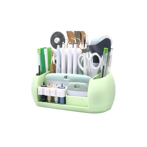 Puede incluir: Un organizador de manualidades verde claro lleno de varias herramientas, incluyendo tijeras, bol&iacute;grafos y cuchillas de corte. El organizador tiene m&uacute;ltiples compartimentos y una bandeja para guardar objetos peque&ntilde;os. Las herramientas est&aacute;n ordenadas.