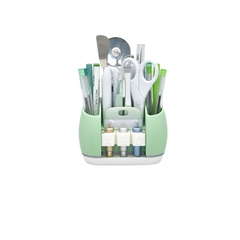 May include: A mint green craft tool organizer filled with various tools, including scissors, pens, and blades. The organizer has a white base and a handle. The tools are arranged neatly, suggesting a focus on organization and crafting.