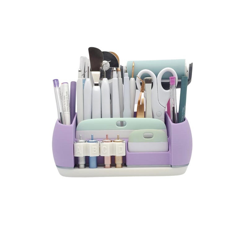 May include: A purple and white craft organizer filled with various tools. The organizer has compartments for pens, scissors, and other crafting supplies. The tools include white handles, gold-colored tweezers, and a light green roller.
