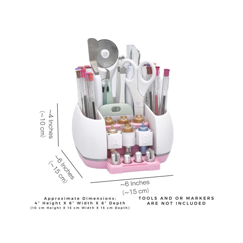 Puede incluir: Un organizador de manualidades blanco y rosa con varias herramientas y rotuladores. El organizador mide aproximadamente 10 cm de alto, 15 cm de ancho y 15 cm de profundidad. El texto de la imagen dice "TOOLS AND OR MARKERS ARE NOT INCLUDED."