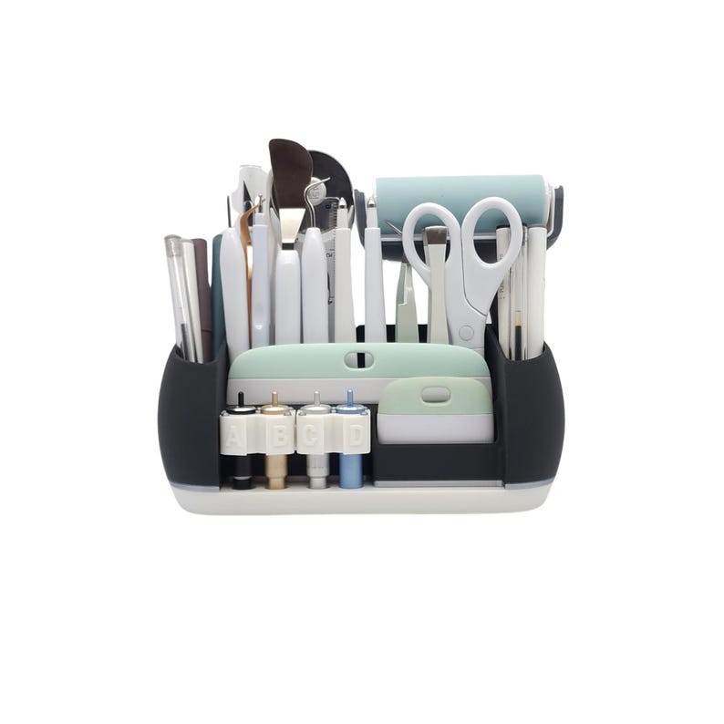 May include: A craft organizer with various tools, including scissors, pens, and spatulas. The organizer is white, black, and mint green, with a roller and a set of tips labeled A, B, C, and D. The tools are arranged neatly, suggesting a crafting or DIY theme.