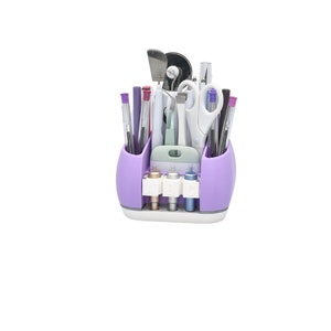 May include: A purple and white craft organizer filled with various tools, including pens, scissors, and cutting tools. The organizer has multiple compartments and a section for storing small accessories. The design is functional and space-saving.