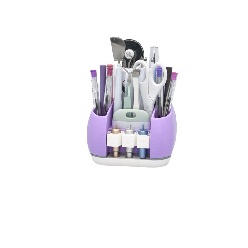 May include: A purple and white craft organizer filled with various tools, including pens, scissors, and cutting tools. The organizer has multiple compartments and a section for storing small accessories. The design is functional and space-saving.