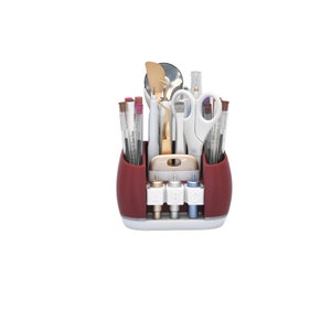May include: A red and white craft organizer filled with various tools. The organizer holds pens, scissors, tweezers, and other crafting implements. The organizer has a white base and a red upper section. The tools are arranged for easy access.
