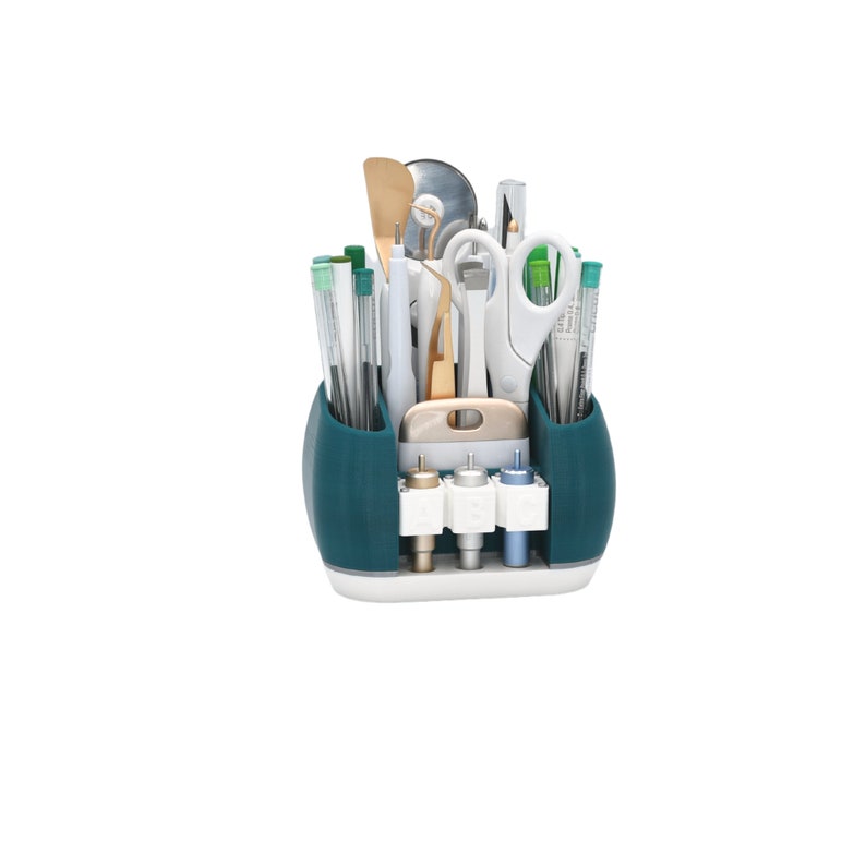 May include: A teal and white craft organizer filled with various tools. The organizer has two side compartments for pens and tools, a center section for other tools, and a bottom section for three different colored tips. Scissors, spatulas, and other tools are visible.