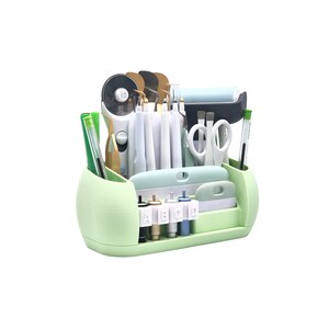 Puede incluir: Un organizador de manualidades verde claro lleno de varias herramientas, incluyendo tijeras, bol&iacute;grafos y cuchillas. El organizador tiene m&uacute;ltiples compartimentos y un soporte incorporado para un rollo de material. Las herramientas est&aacute;n ordenadas.