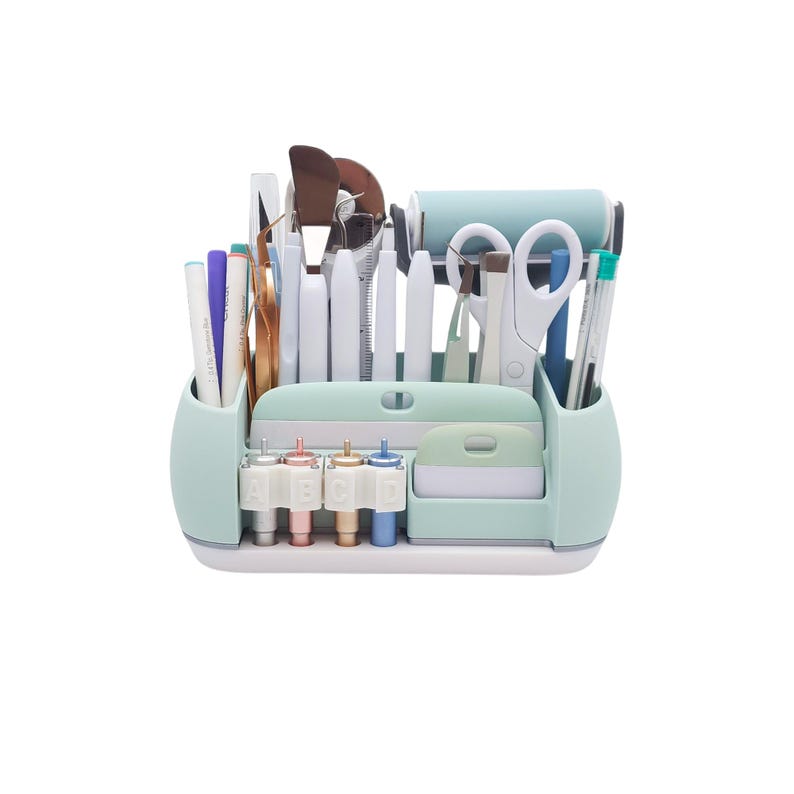 May include: A mint green craft organizer filled with various tools, including pens, scissors, spatulas, and a roller. The organizer has multiple compartments and a white base, perfect for storing craft supplies.