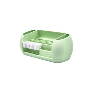 Puede incluir: Un organizador de escritorio verde claro con m&uacute;ltiples compartimentos. Cuenta con una secci&oacute;n para bol&iacute;grafos, un caj&oacute;n peque&ntilde;o y un soporte con las letras A, B, C y D. El organizador tiene un dise&ntilde;o redondeado con dos soportes laterales.