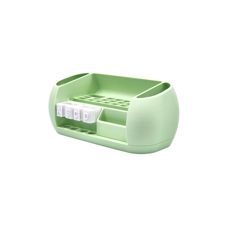 Puede incluir: Un organizador de escritorio verde claro con m&uacute;ltiples compartimentos. Cuenta con una secci&oacute;n para bol&iacute;grafos, un caj&oacute;n peque&ntilde;o y un soporte con las letras A, B, C y D. El organizador tiene un dise&ntilde;o redondeado con dos soportes laterales.