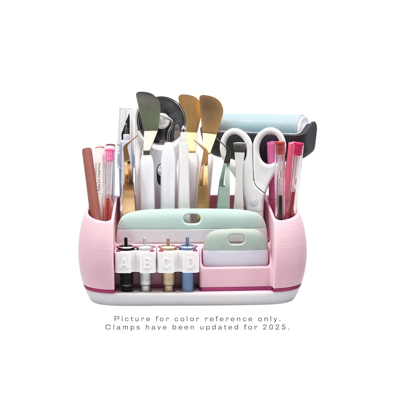 May include: A pink and mint green craft organizer filled with various tools, including scissors, spatulas, and pens. The organizer has multiple compartments and a white base. Text on the organizer reads "A B C D". The text at the bottom reads "Picture for color reference only. Clamps have been updated for 2025."