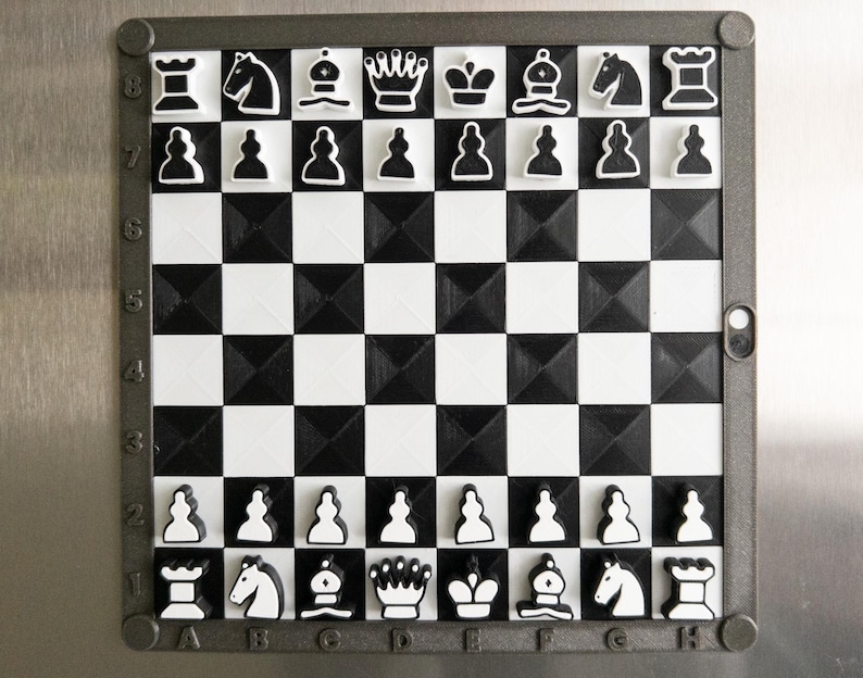 May include: A black and white magnetic chess set with a 3D textured board. The set includes all the standard chess pieces, including pawns, rooks, knights, bishops, queens, and kings. The board is numbered 1-8 and lettered A-H.