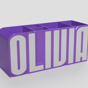 May include: A purple desk tidy with the name "OLIVIA" in large white letters. The organiser has several compartments for storing pens, pencils, and other desk supplies. The design is modern and sleek.