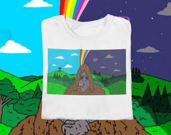 Op de afbeelding: Wit t-shirt met een cartoon illustratie van een Bigfoot-achtig wezen dat een sigaret rookt. De afbeelding is verdeeld, met een dagscène aan de linkerkant en een nachtscène aan de rechterkant, verbonden door een regenboog. Groene heuvels en blauwe luchten zijn zichtbaar.