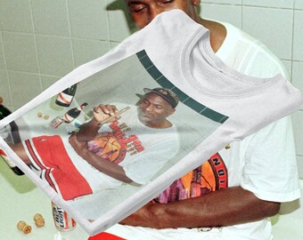 Op de afbeelding: Wit T-shirt met een bedrukte afbeelding van Michael Jordan die een wit T-shirt draagt met de tekst "Chicago Bulls" en een sigaar vasthoudt. De afbeelding is tegen een groene achtergrond.