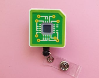 May include: A green circuit board badge reel with a black retractable cord and a clear plastic clip. The circuit board has a small black square in the center.