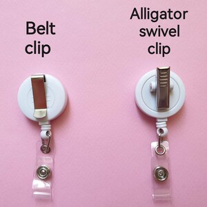 May include: Two white retractable badge holders with different clips. The left holder has a belt clip and the right holder has an alligator swivel clip. Both holders have a clear plastic strap.