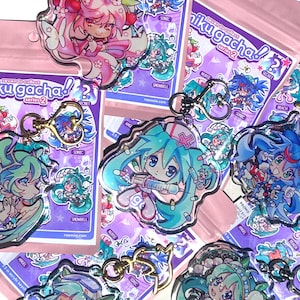 Puede incluir: Varios llaveros acrílicos con diseños de personajes de estilo anime y colores vibrantes. Cada llavero tiene un cierre dorado y viene empaquetado con una bolsa rosa que dice "miku gacha! series 2". Los personajes tienen varios diseños y colores.