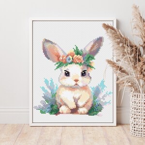 Könnte beinhalten: Ein weißes Kaninchen mit einer Blumenkrone sitzt in einem Feld mit blauen und grünen Blumen. Das Kaninchen hat braune Augen und eine rosa Nase.