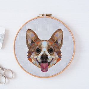 May include: Cross-stitch pattern of a dog's face. The dog has brown, white, and black fur. The dog is smiling with its tongue sticking out.