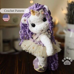 May include: Crochet pattern for a purple and white unicorn doll wearing a tulle skirt with gold stars. The doll has a purple bow in its hair and a gold horn. The pattern is available as a PDF download.