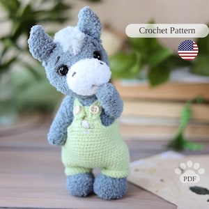 Puede incluir: Patrón de crochet para un burro gris y blanco que lleva un mono verde. El patrón está disponible para descargar en PDF.
