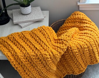 May include: A mustard yellow crocheted throw blanket draped over a wicker basket.