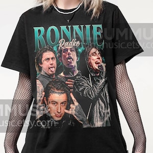 May include: Black t-shirt with a vintage-style graphic of Ronnie Radke, the lead singer of the band Falling in Reverse. The graphic features four images of Radke in different poses, with the text "Ronnie Radke" in a teal blue font.