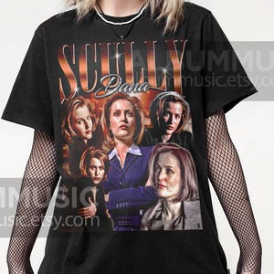 Op de afbeelding: Zwart T-shirt met een grafische print van Dana Scully uit The X-Files. De grafiek is een collage van verschillende afbeeldingen van Scully, waaronder een close-up van haar gezicht en een foto van haar in een pak. De tekst "Scully Dana" is gedrukt in grote, vetgedrukte letters boven de collage.