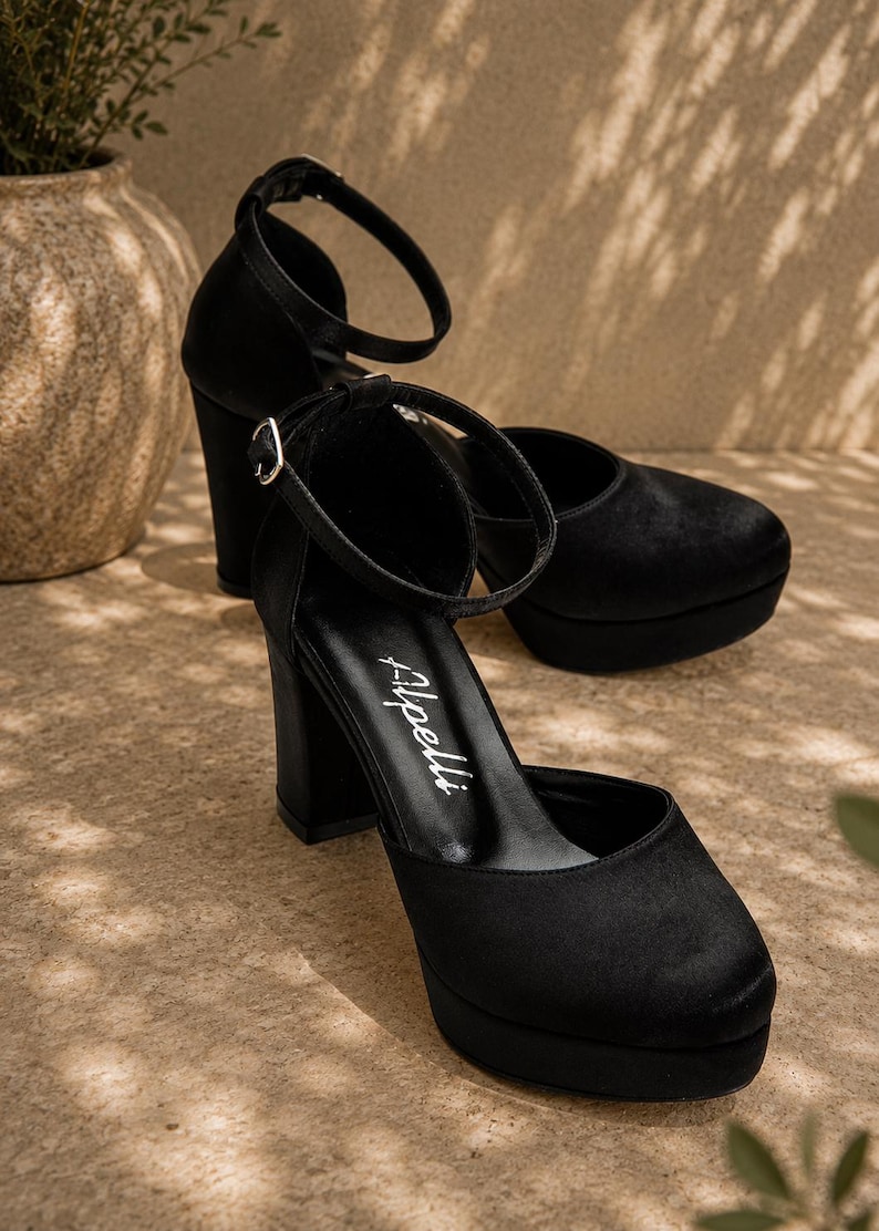 May include: Black platform heels with ankle straps. The shoes have a rounded toe and a thick block heel. The brand name "Apelli" is visible on the insole. The shoes are made of a soft, velvety material.