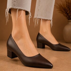 Peut inclure: Escarpins en cuir marron fonc&eacute; &agrave; bout pointu et talon bloc. Les chaussures sont port&eacute;es avec un jean en denim clair avec des ourlets effiloch&eacute;s. Les talons mesurent environ 5 cm de haut.