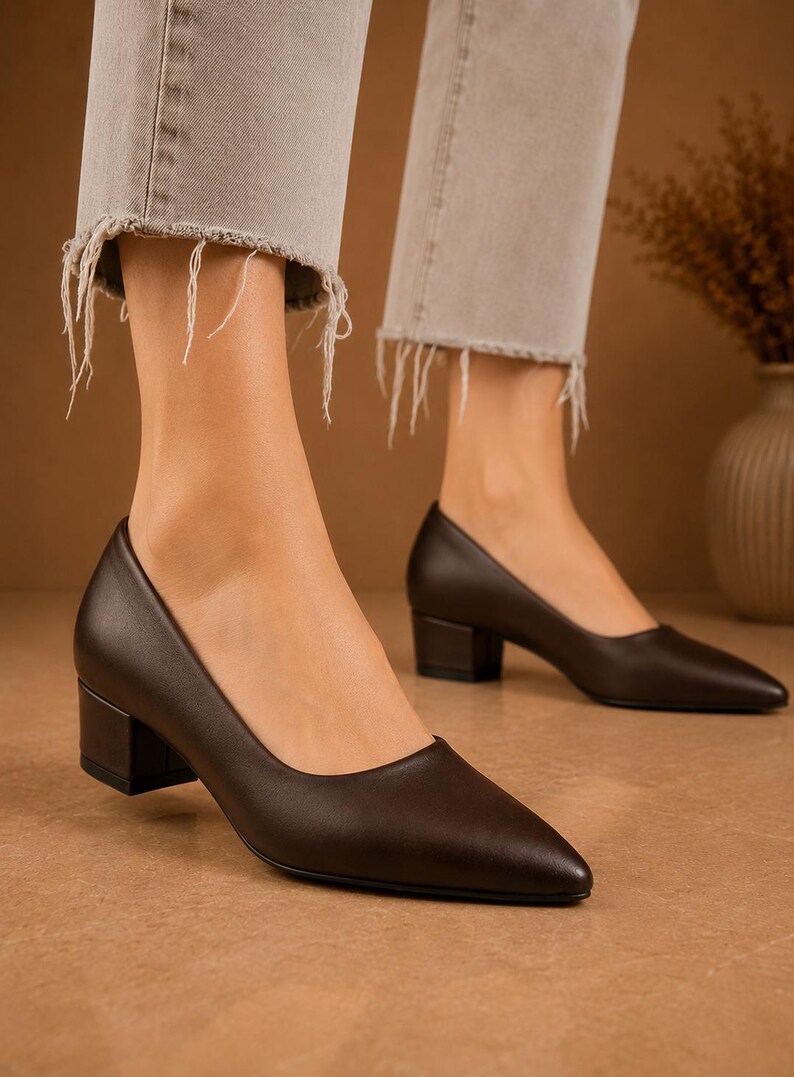 Peut inclure: Escarpins en cuir marron fonc&eacute; &agrave; bout pointu et talon bloc. Les chaussures sont port&eacute;es avec un jean en denim clair avec des ourlets effiloch&eacute;s. Les talons mesurent environ 5 cm de haut.