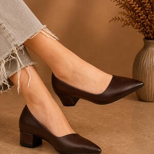 Peut inclure: Escarpins en cuir marron fonc&eacute; avec un bout pointu et un talon bloc. Les chaussures sont de couleur marron fonc&eacute; et ont un design classique et &eacute;l&eacute;gant. Les talons mesurent environ 5 cm de haut.