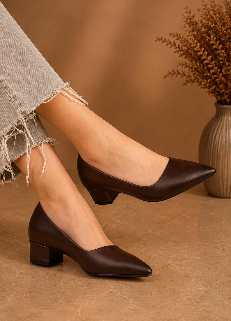 Peut inclure: Escarpins en cuir marron fonc&eacute; avec un bout pointu et un talon bloc. Les chaussures sont de couleur marron fonc&eacute; et ont un design classique et &eacute;l&eacute;gant. Les talons mesurent environ 5 cm de haut.