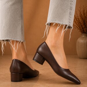 Peut inclure: Escarpins en cuir marron fonc&eacute; avec un bout pointu et un talon bloc. Les chaussures sont port&eacute;es avec un jean en denim gris clair avec des ourlets effiloch&eacute;s. Les talons mesurent environ 5 cm de haut.