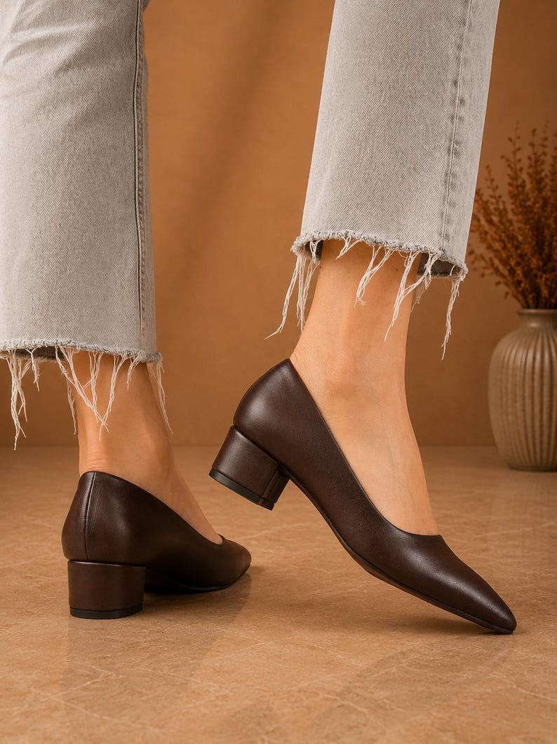 Peut inclure: Escarpins en cuir marron fonc&eacute; avec un bout pointu et un talon bloc. Les chaussures sont port&eacute;es avec un jean en denim gris clair avec des ourlets effiloch&eacute;s. Les talons mesurent environ 5 cm de haut.
