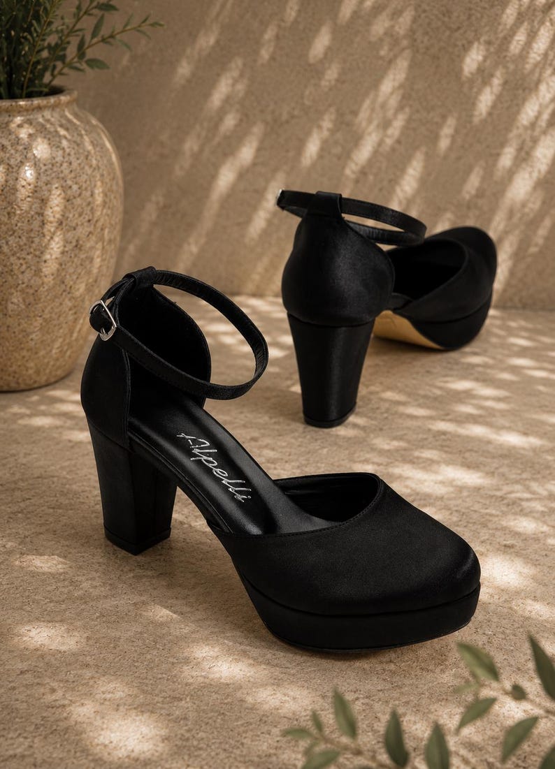 May include: Black platform heels with ankle straps. The shoes have a rounded toe and a thick, block heel. The heels are approximately 10 cm high. The shoes are made of a smooth, satin-like material.