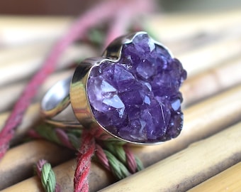 May include: A silver ring featuring a heart-shaped amethyst gemstone. The amethyst is a cluster of small crystals, giving it a rough, natural appearance.