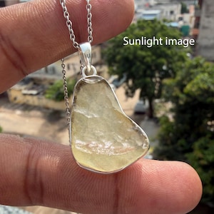 May include: A pendant necklace featuring a translucent, pale yellow, irregular-shaped stone set in a silver-coloured metal frame. The pendant hangs from a silver-coloured chain. The text "Sunlight image" is visible in the upper right corner.