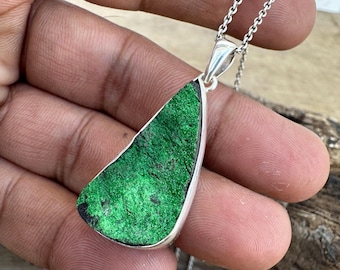 May include: A silver pendant necklace with a green gemstone. The gemstone is a teardrop shape and has a rough, natural texture.