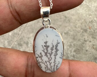 May include: An oval-shaped pendant featuring a white stone with dark, branching, tree-like dendrite inclusions. The stone is set in a polished silver bezel and hangs from a delicate silver chain, creating a clean and refined jewelry piece.