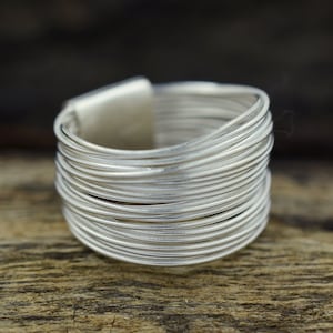 May include: A silver ring made of multiple thin wires wrapped around each other. The ring is thick and wide.