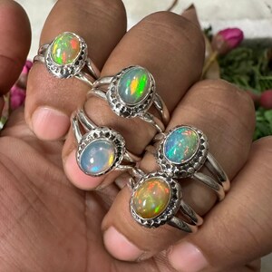Puede incluir: Cinco anillos de plata con piedras preciosas de ópalo de forma ovalada. Los ópalos son iridiscentes con tonos de verde, azul y naranja.